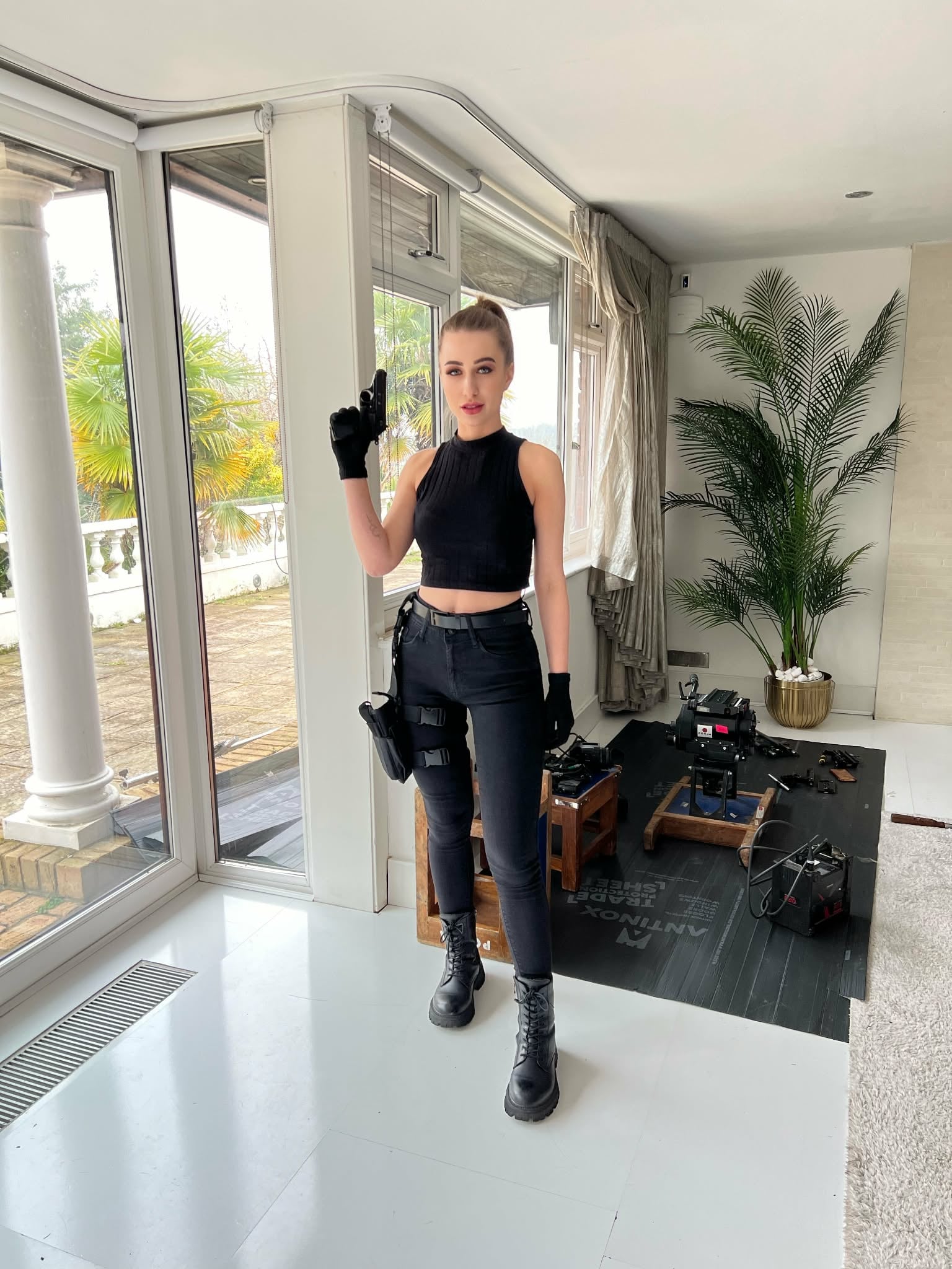 Iryna Vyacheslavivna wearing a black cropped top, trousers, gloves, and boots indoors