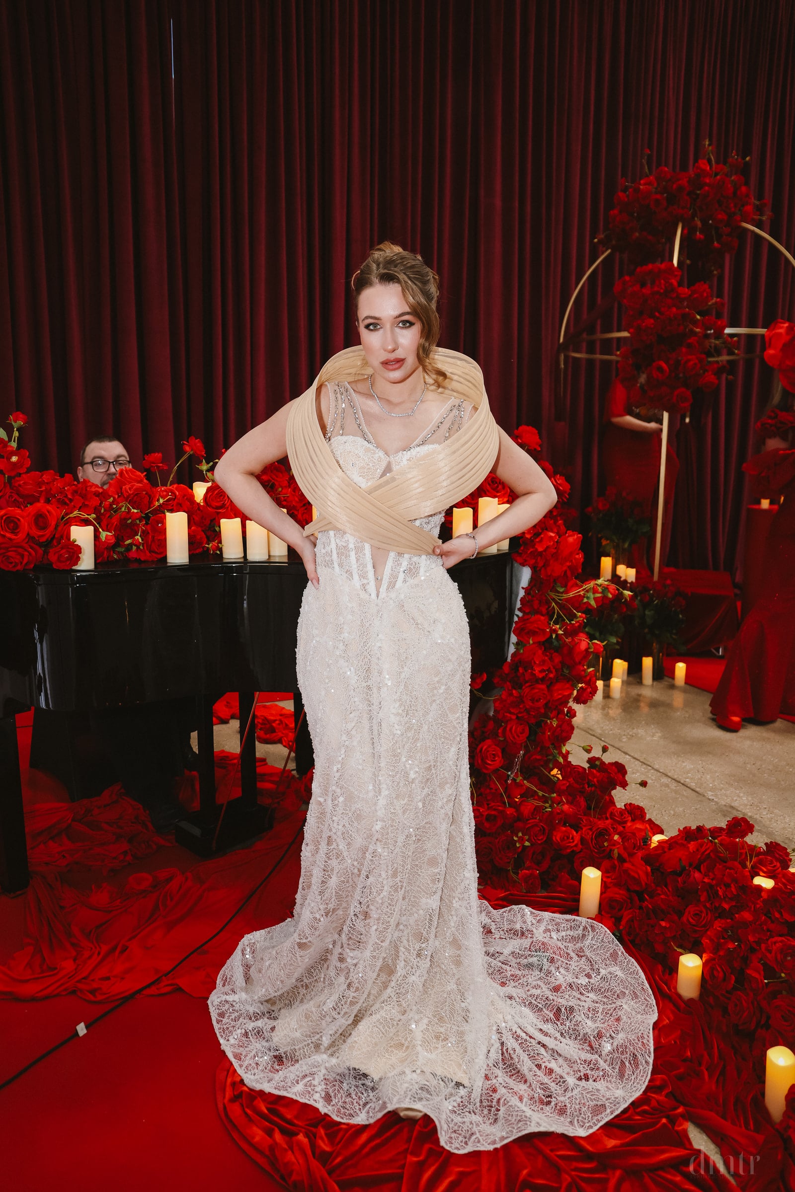 Iryna Vyacheslavivna in a white lace gown on a stage surrounded by red flowers